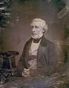 James Gordon Bennett, three-quarter length portrait, three-quarters to the left, seated, hands folded in lap, seated beside a small table with tablecloth on which rests a tall hat (between 1851 and 1852; LOC: LC-USZC4-4150)