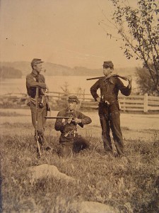 Three unidentified young soldiers in uniforms with shotguns, musket, and pipes in a field with a fence in the background (between 1861 and 1865; LOC: LC-DIG-ppmsca-27555)