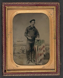 Unidentified sailor in Union uniform resting hand on American flag-draped table in front of painted backdrop showing naval scene (between 1861 and 1865; LOC: LC-DIG-ppmsca-36955)
