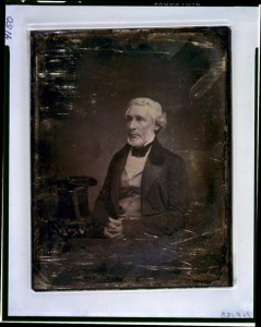 James Gordon Bennett, three-quarter length portrait, three-quarters to the left, seated, hands folded in lap, seated beside a small table with tablecloth on which rests a tall hat (between 1851 and 1852; LOC: LC-USZC4-4150)