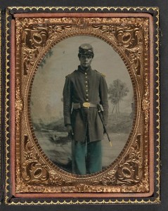 Unidentified African American soldier in Union uniform and Company B, 103rd Regiment forage cap with bayonet and scabbard in front of painted backdrop showing landscape with river] (between 1863 and 1865; LOC: LC-DIG-ppmsca-36988)