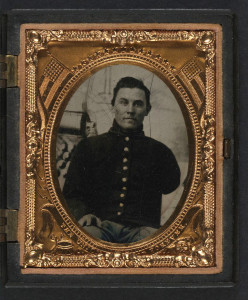 Unidentified soldier with amputated arm in Union uniform in front of painted backdrop showing cannon and cannonballs (between 1861 and 1865; LOC: LC-DIG-ppmsca-27369)