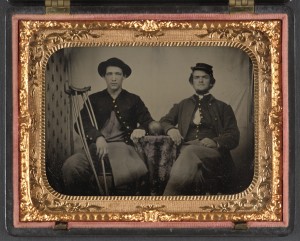 [Two unidentified soldiers in Union private's uniforms sitting next to table with cannon ball on top; one soldier has an amputated leg and holds crutches] (between 1861 and 1865; LOC: https://www.loc.gov/item/2012648229/)